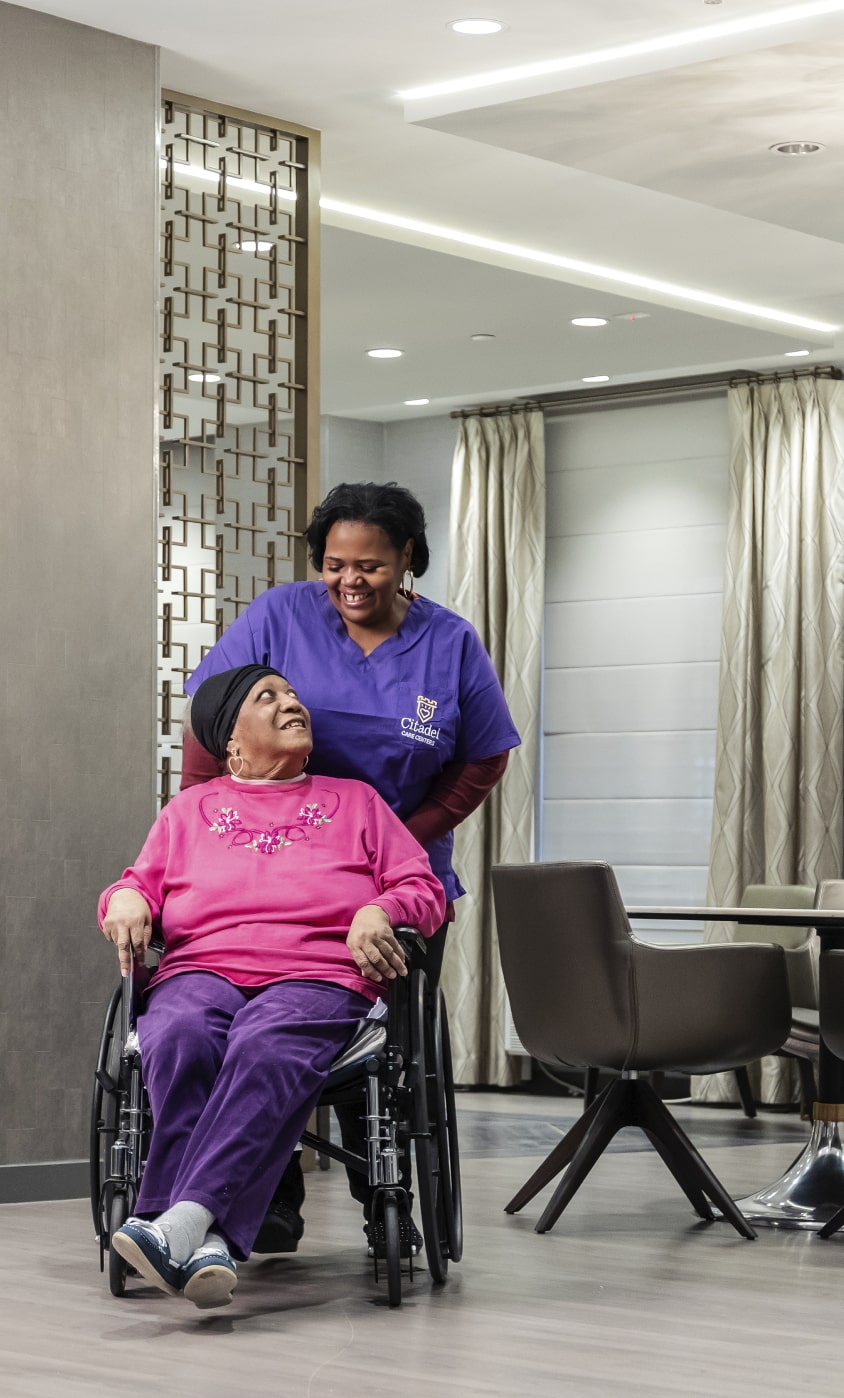 Skilled nurse wheeling elderly resident in nursing home
